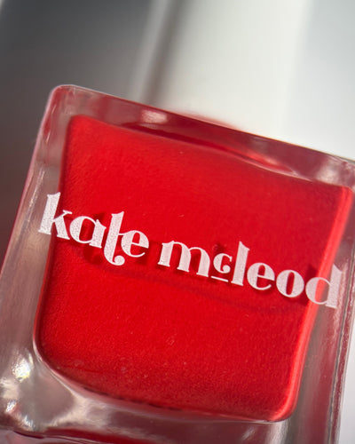 Red nail polish bottle with 'kate mcLeod' branding on a clear base.