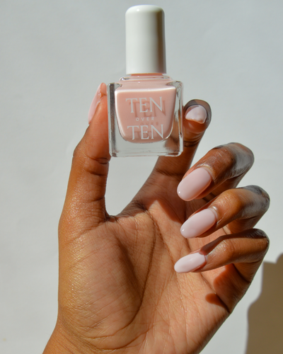 Hand holding a bottle of Tenoverten nail polish in a pale pink color.