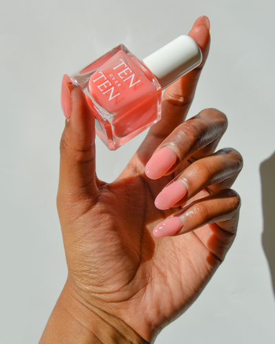 Hand holding a bottle of Tenoverten nail polish in a sheer pink color.