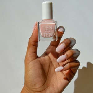 Hand holding a bottle of Tenoverten nail polish in a pale pink color. 