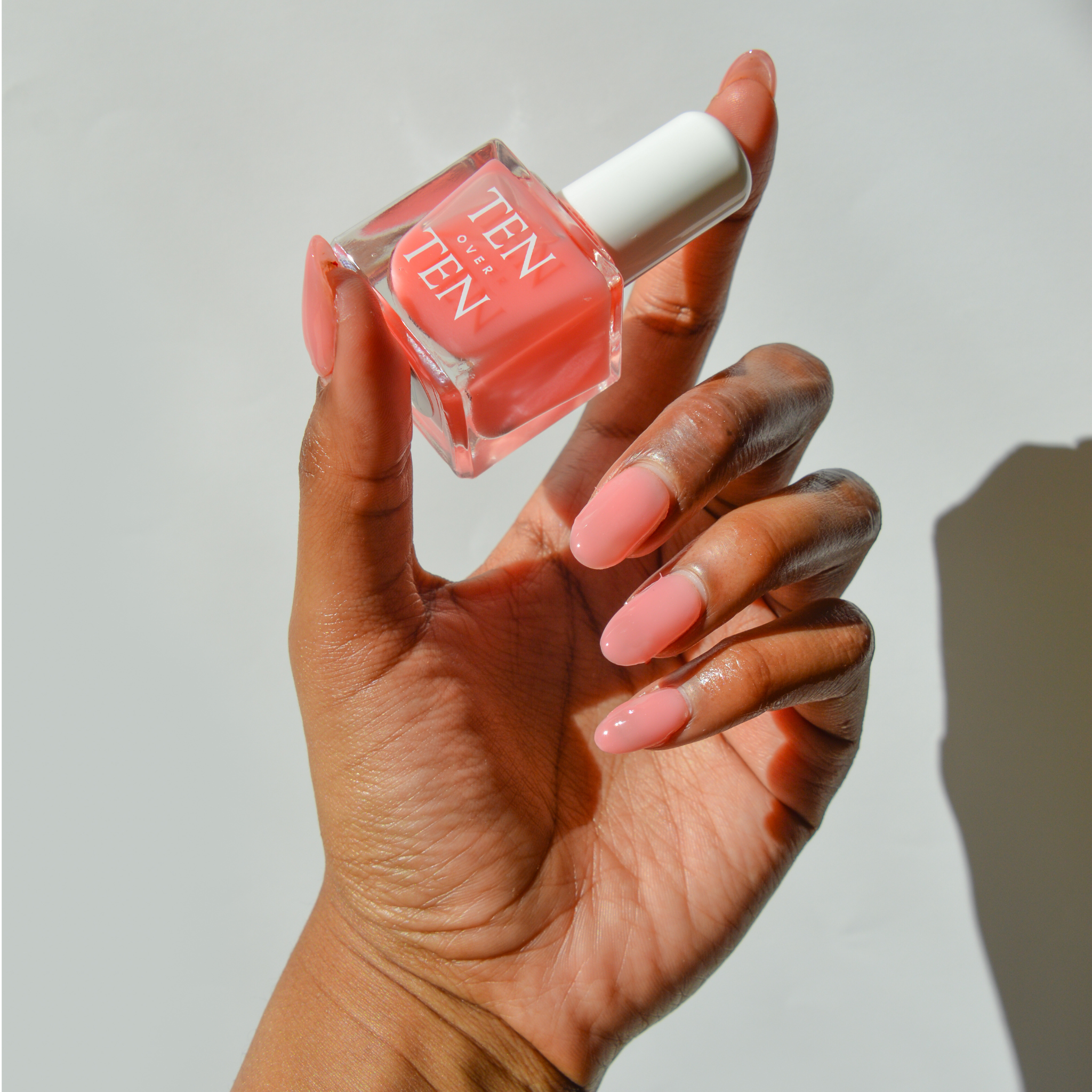 Hand holding a bottle of Tenoverten nail polish in a sheer pink color. 
